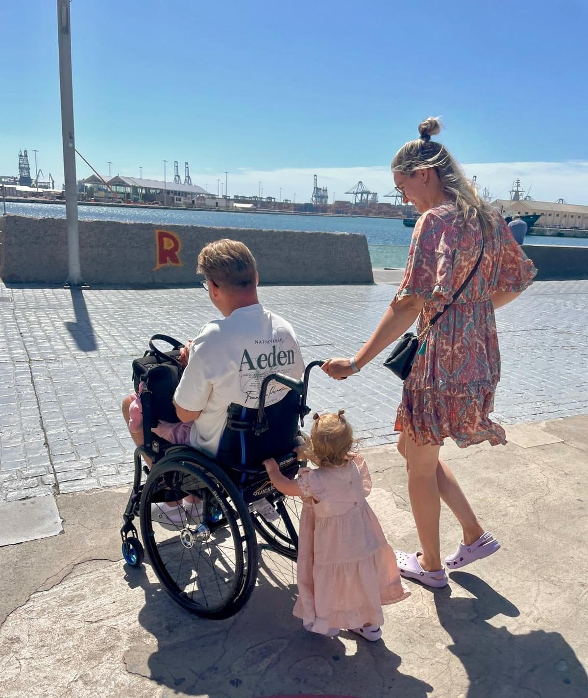 Davey in zijn rolstoel wandelt met Gaia en hun dochter over de kade langs het water. De oprichters van AccessProof.