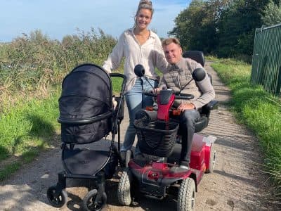 Davey in zijn rolstoel en Gaia wandelen met de kinderwagen over een groen pad.